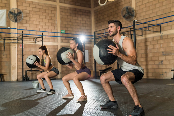 Volledige lengte van knappe sportman die traint met sportvrouwen tijdens cross training in een fitnessclub - Foto, afbeelding