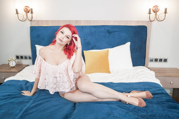 portret van mooie verleidelijke jonge vrouw in roze sexy lingerie liggend in blauw bed - Foto, afbeelding