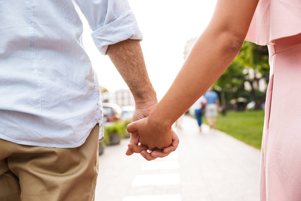 Couple walking by street outdoors holding hands of each other. - 写真・画像