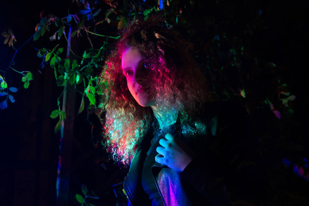 Girl in blond curly hair, illuminated by multi-colored light. - Zdjęcie, obraz