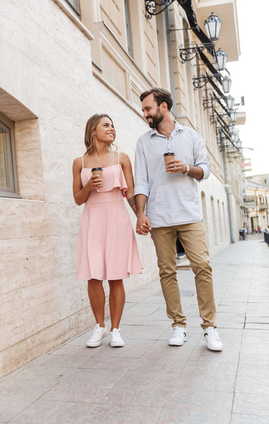 Young loving couple outdoors walking drinking coffee. - Fotó, kép