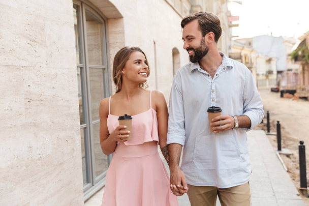 Young loving couple outdoors walking drinking coffee. - Foto, Imagen
