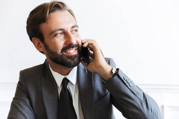 Image closeup of smiling satisfied businessman talking on cellphone while working in office - Foto, Imagem