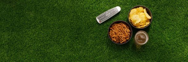 Snacks and TV remote control on a green lawn. View from above. The apartment was lying. The concept of football matches. - Foto, imagen