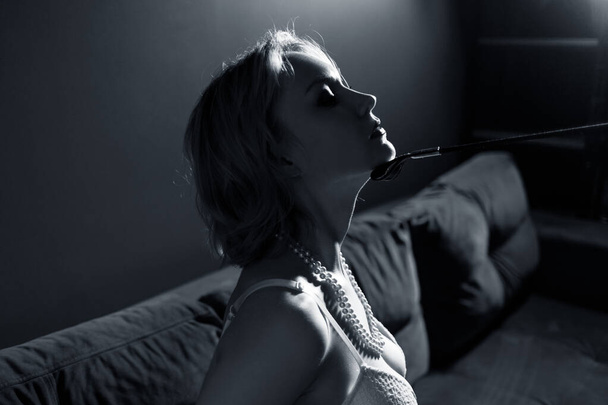 Blonde submissive woman with leather whip touches her chin. - Fotografie, Obrázek