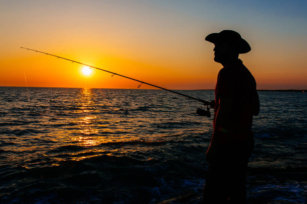 Silhouette di Pescatore in piedi e lanciare una canna da pesca durante la pesca al mare nella stagione estiva. Questo pescatore sulle rocce e in riva al mare. Pesca sotto il cielo blu pulito e l'oceano
 - Foto, immagini