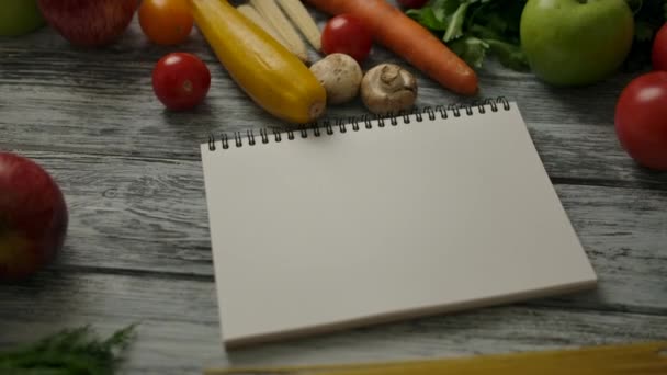 Bloc de notas en blanco en medio de la comida vegana en la mesa - Imágenes, Vídeo