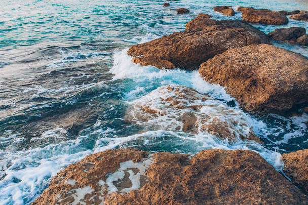 Błękitny ocean lub błękitne morze, fale i skały. Turkusowe fale morskie rozbijają się i uderzają o skały na wybrzeżu lub brzegu oceanu lub morza. Piękny krajobraz malowniczej przyrody. - Zdjęcie, obraz