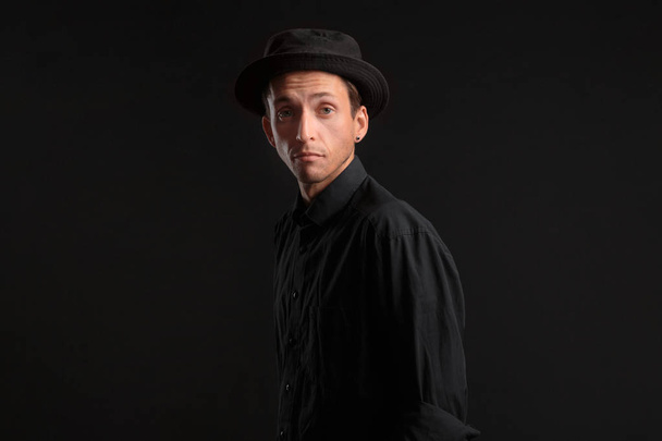 Stylish handsome man a black shirt and pork pie hat isolated over black background. Low key portrait. - Photo, Image