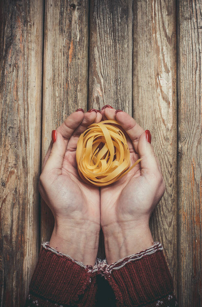 Raw pasta in the hands of a girl for cooking pasta on a wooden background - Foto, Bild