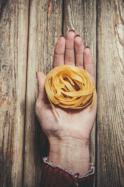 Raw pasta in the hands of a girl for cooking pasta on a wooden background - Фото, изображение