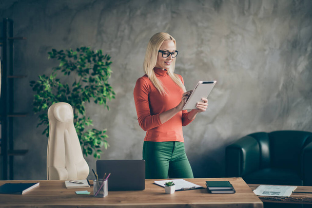Portrait of confident cool leader woman stand in her office loft work on tablet reading start-up news wear red turtleneck green pants trousers - Foto, Imagem