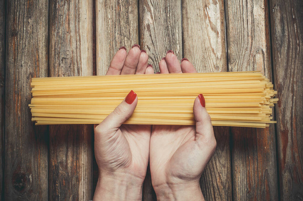 Raw pasta in the hands of a girl for cooking pasta on a wooden background - Фото, изображение