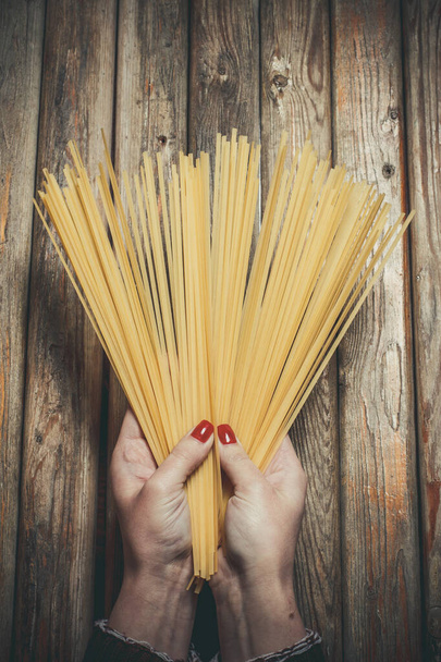 Raw pasta in the hands of a girl for cooking pasta on a wooden background - Valokuva, kuva