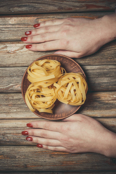 Raw pasta in the hands of a girl for cooking pasta on a wooden background - Foto, Bild