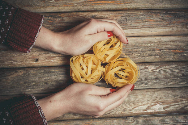 Raw pasta in the hands of a girl for cooking pasta on a wooden background - Zdjęcie, obraz