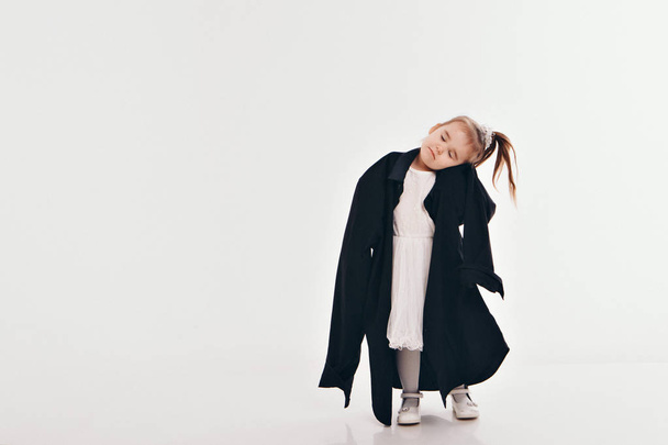 a little girl tries on dad's shirt. Child in big black clothes on white background. Concept of children's games, imitation of adult life, fashion - Photo, image