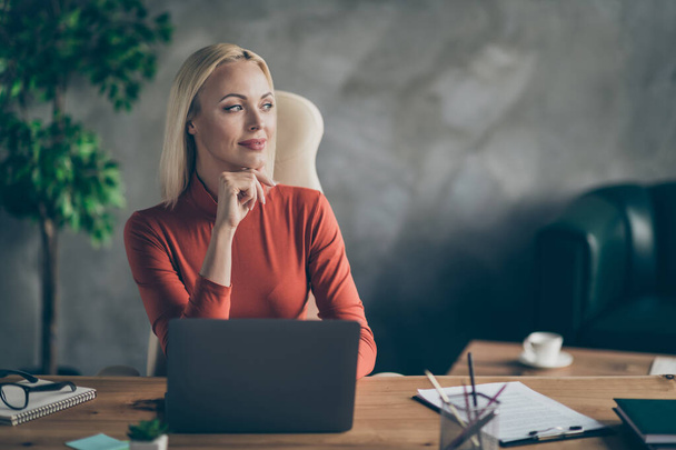 Photo of cheerful cute dreamy woman looking far away in search of new ideas for startup sitting at table with laptop on it - Fotografie, Obrázek