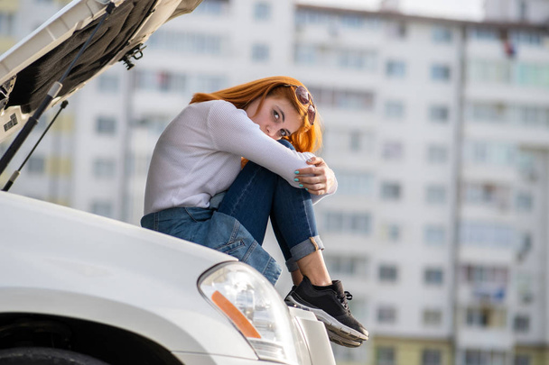 Genç, stresli kadın sürücü, kırık kapüşonlu arabanın yanında. - Fotoğraf, Görsel