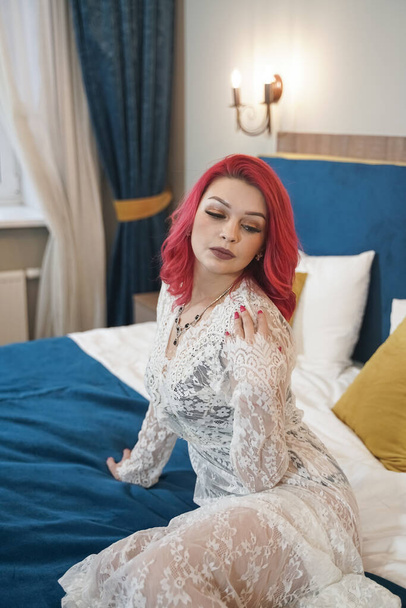 beautiful bride girl with red bob haircut in lace long dress posing in her bedroom alone - Foto, immagini