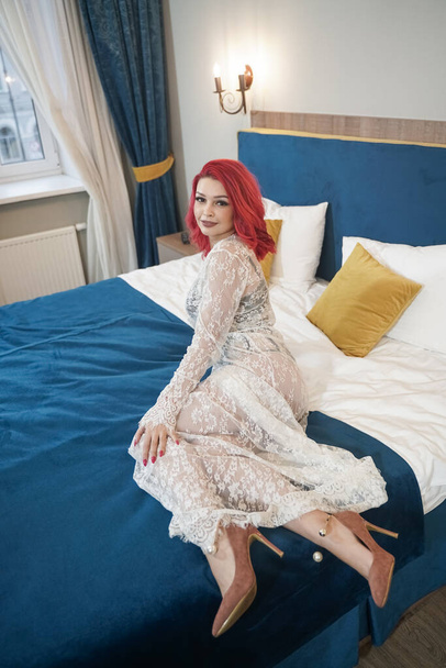 beautiful bride girl with red bob haircut in lace long dress posing in her bedroom alone - Photo, Image
