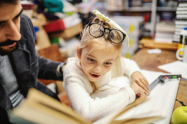 Roztomilý malý kavkazský blond dívka bez dvou zubů čtení knihy s jeho starostlivý otec v knihkupectví. - Fotografie, Obrázek