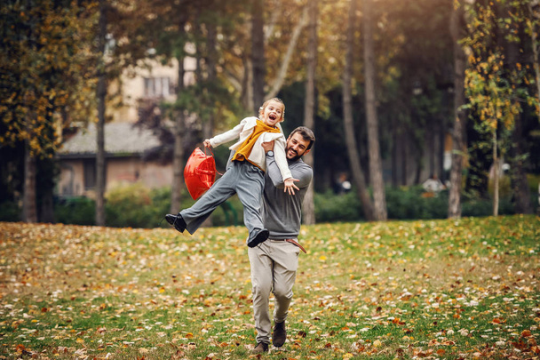 Leikkisä huolehtiva isä juoksee ja nostaa tyttärensä puistossa. Tyttö pitelee ilmapalloa ja nauraa. Laadukas perheaika
. - Valokuva, kuva