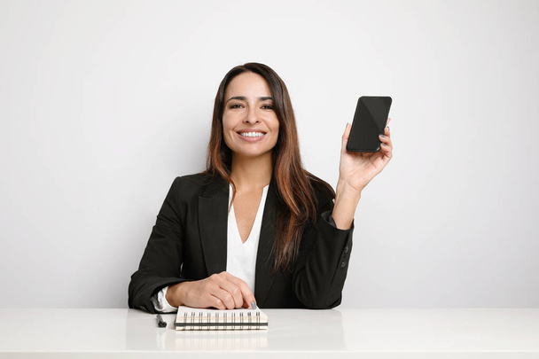 Office secretary young lady posing on the white wall and showing her smartphone. Co-working. - Foto, imagen