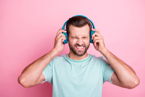 Frustrated man feeling anger cant suffer loud stereo music from his modern blue wireless headset have headache close eyes wear casual style clothing isolated over pink color background - Photo, image