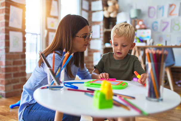 Mladé bělošské dítě hrající si s učitelkou na škole. Matka a syn v herně kreslit remízu s barevnými tužkami - Fotografie, Obrázek