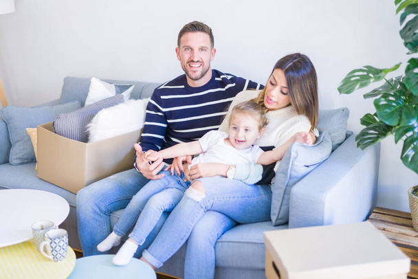 Hermosa familia, padres sentados en el sofá bebiendo café mirando a su hijo jugando en un nuevo hogar alrededor de cajas de cartón
 - Foto, Imagen