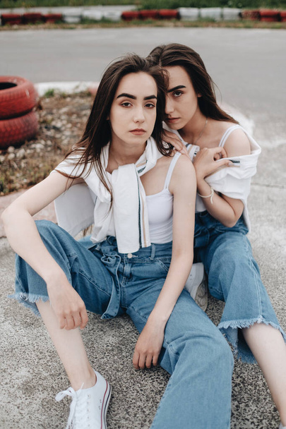 Portré két fiatal barna ikrek nővérek öltözött Alike farmer és fehér póló, legjobb barátok Forever Concept - Fotó, kép
