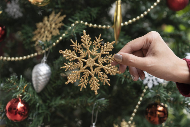 Hand houden gouden sneeuwvlok decoraties op kerstboom achtergrond. voor Kerstmis en Gelukkig Nieuwjaar 2020.  - Foto, afbeelding
