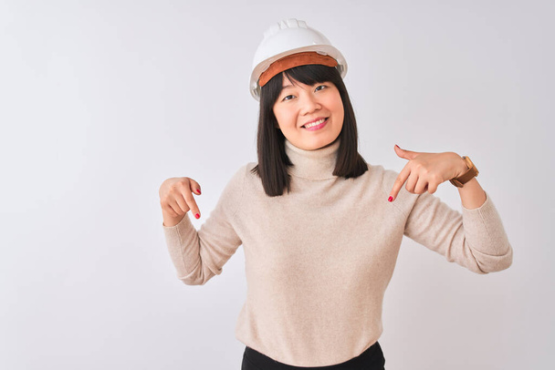 Jovem bela arquiteta chinesa mulher usando capacete sobre fundo branco isolado olhando confiante com sorriso no rosto, apontando-se com os dedos orgulhosos e felizes
. - Foto, Imagem