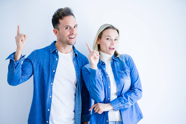 Young beautiful couple wearing denim shirt standing over isolated white background pointing finger up with successful idea. Exited and happy. Number one. - Фото, зображення