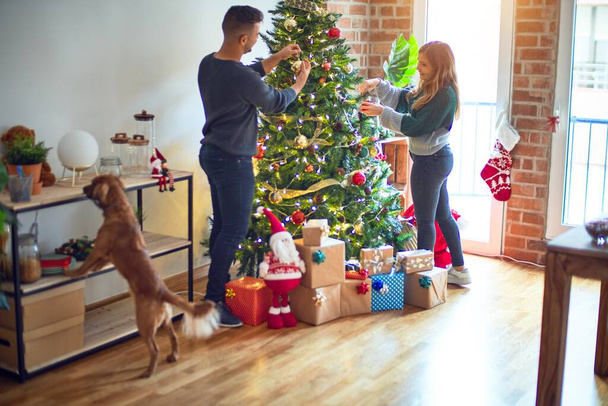 Young beautiful couple smiling happy and confident. Standing and decoring christmas tree at home - Φωτογραφία, εικόνα