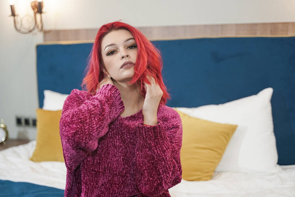 Beautiful young red haired woman in warm oversize sweater on the bed - Photo, Image