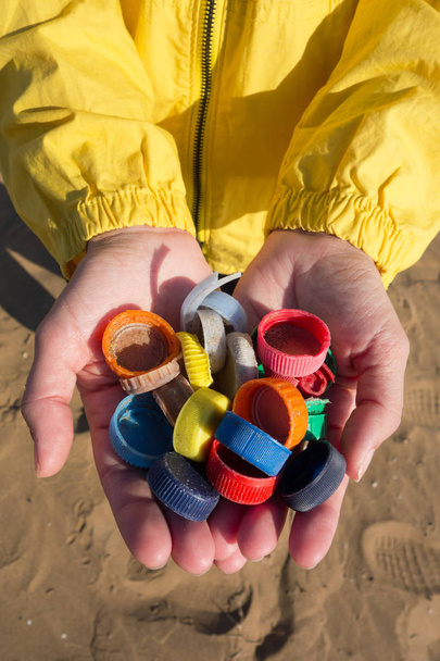 Ręce pełne plastikowych zatyczek zebranych na plaży. Koncepcja zanieczyszczenia plastycznego oceanu. - Zdjęcie, obraz