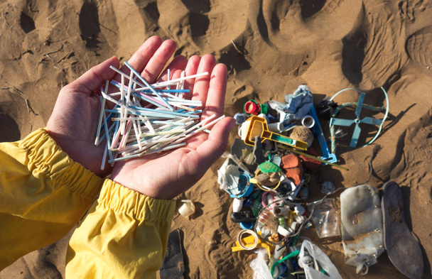 Hände voller Ohrstöpsel und anderen Plastikmüll, die am Strand gesammelt wurden. Konzept zur Plastikverschmutzung der Ozeane. - Foto, Bild