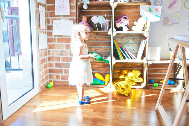 Αξιολάτρευτο ξανθό νήπιο παίζει γύρω από πολλά παιχνίδια στο νηπιαγωγείο - Φωτογραφία, εικόνα