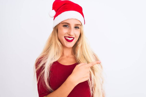 Young beautiful woman wearing Christmas Santa hat over isolated white background cheerful with a smile of face pointing with hand and finger up to the side with happy and natural expression on face - Photo, Image