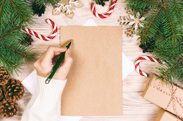 Kobiece ręce piszą list do Świętego Mikołaja. Prezenty świąteczne na drewnianym tle. Widok z góry. Warzywa - Zdjęcie, obraz