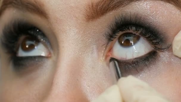 Μοντέλο με καστανά μάτια εφαρμογή eyeliner κινηματογράφηση σε πρώτο πλάνο. Επαγγελματικό μακιγιάζ καλλιτέχνης εφαρμόζοντας μαύρο eyeliner. Καιρό ψεύτικες βλεφαρίδες - Πλάνα, βίντεο