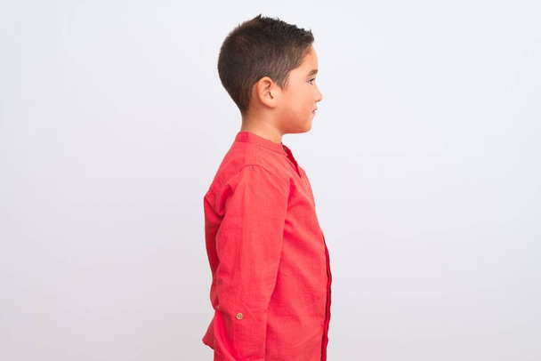 Menino bonito vestindo camisa vermelha elegante em pé sobre fundo branco isolado olhando para o lado, relaxar pose perfil com rosto natural com sorriso confiante
. - Foto, Imagem