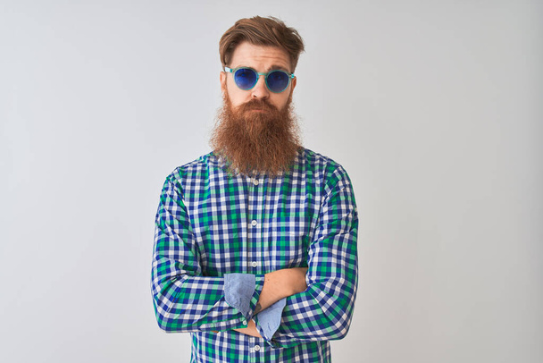 Young redhead irish man wearing casual shirt and sunglasses over isolated white background skeptic and nervous, disapproving expression on face with crossed arms. Negative person. - Valokuva, kuva