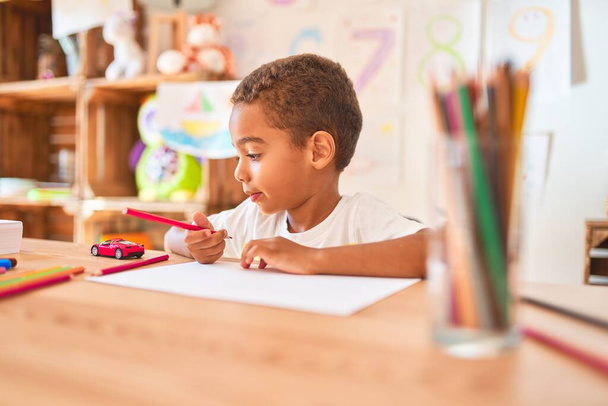 Gyönyörű afro-amerikai kisgyerek ül rajz segítségével papír és ceruza az asztalon óvoda - Fotó, kép