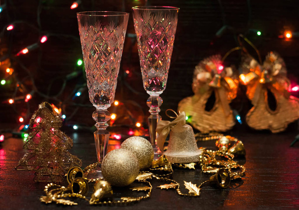Golden Christmas balls, bells, crystal glasses on a dark background. rear multi-colored flashlights. bokeh background - Photo, Image