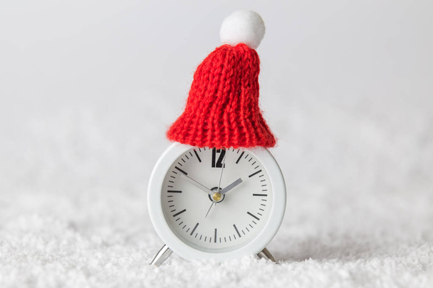 Small analog clock with hat in snow abstract. Winter season and christmas time concept. - Foto, Imagen
