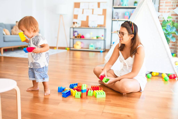 Belle enseignante et tout-petit jouant avec des blocs de construction autour de beaucoup de jouets à la maternelle
 - Photo, image