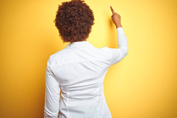 Африканская американская деловая женщина на изолированном жёлтом фоне позирует назад, указывая пальцем вперед.
 - Фото, изображение